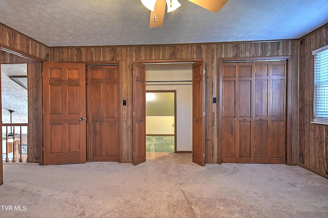 unfurnished bedroom with light colored carpet, a textured ceiling, and wood walls