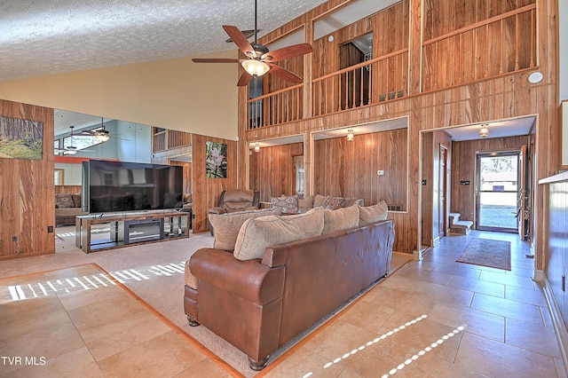 tiled living room featuring high vaulted ceiling, a textured ceiling, ceiling fan, and wood walls