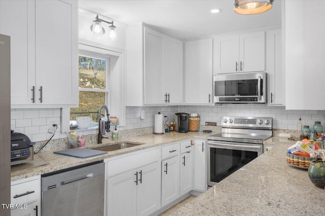 kitchen with sink, white cabinetry, tasteful backsplash, light stone counters, and appliances with stainless steel finishes