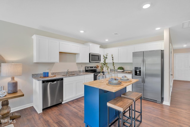 kitchen with sink, appliances with stainless steel finishes, white cabinetry, dark hardwood / wood-style floors, and a kitchen bar