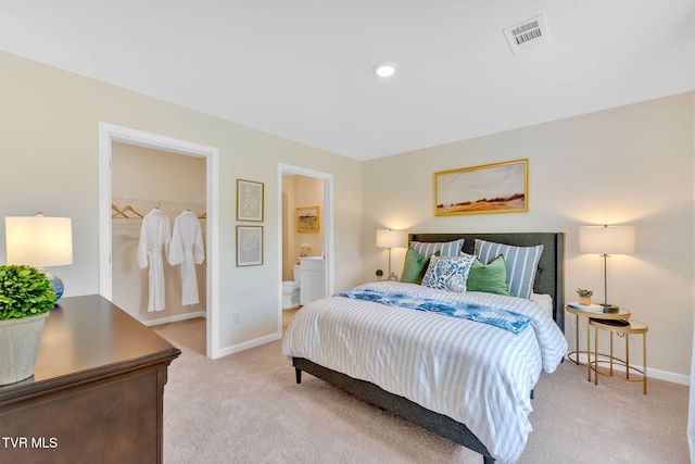 bedroom featuring a walk in closet, light carpet, and ensuite bath