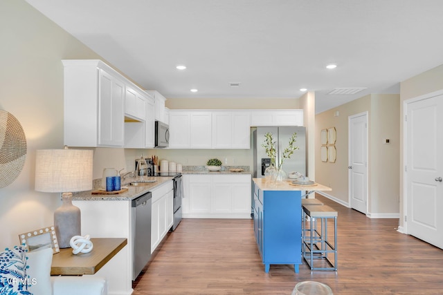 kitchen with white cabinetry, appliances with stainless steel finishes, a kitchen breakfast bar, hardwood / wood-style flooring, and light stone countertops