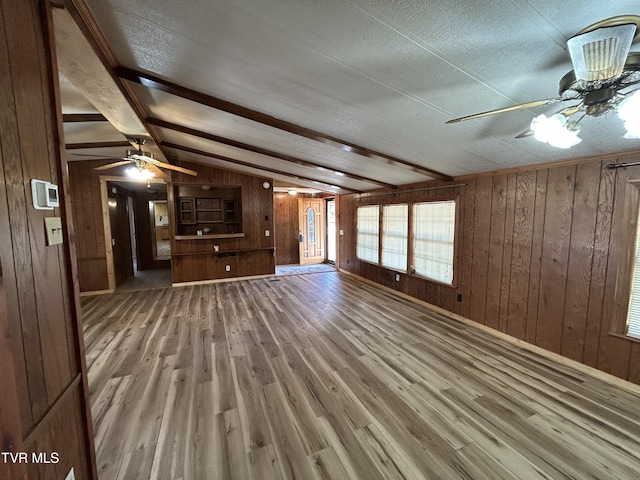 unfurnished living room with ceiling fan, wood-type flooring, wooden walls, and lofted ceiling with beams