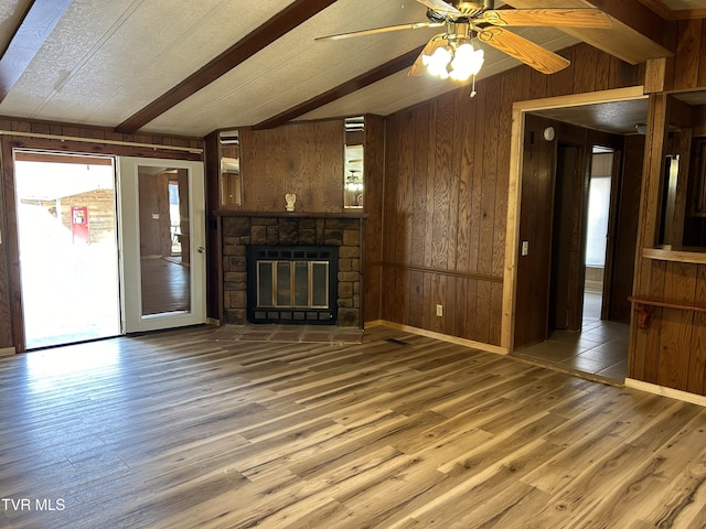 unfurnished living room featuring a stone fireplace, wood walls, lofted ceiling with beams, wood-type flooring, and ceiling fan