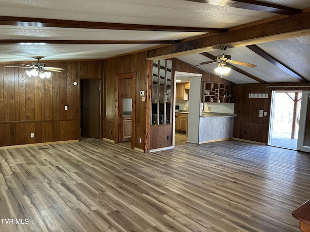 unfurnished living room featuring hardwood / wood-style flooring, ceiling fan, wooden walls, and lofted ceiling with beams