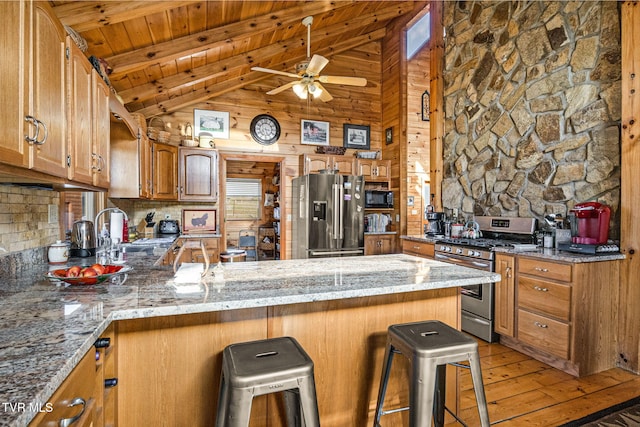 kitchen featuring a kitchen bar, kitchen peninsula, stone counters, and appliances with stainless steel finishes