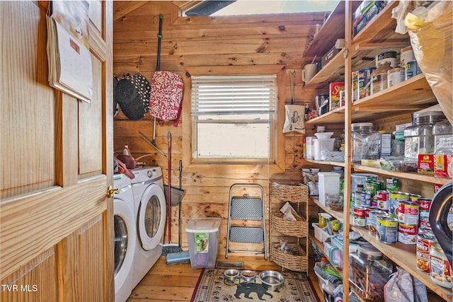 clothes washing area with wooden walls, separate washer and dryer, and light wood-type flooring