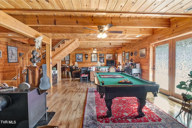 game room featuring beam ceiling, a wood stove, wooden ceiling, and wooden walls