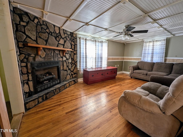 living room featuring a stone fireplace, wood-type flooring, and ceiling fan