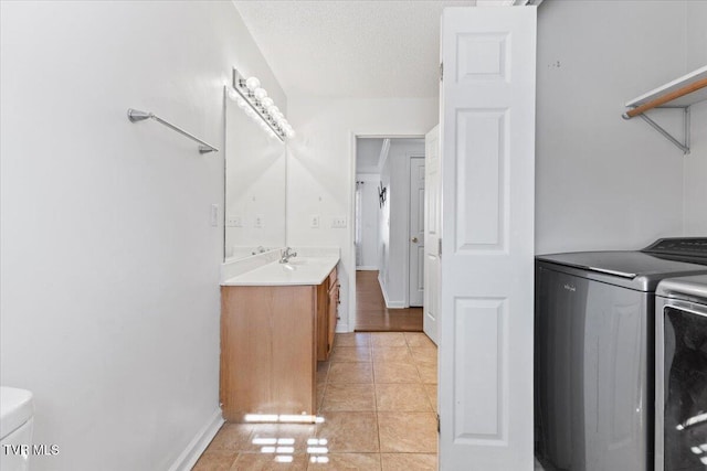 washroom with sink, washing machine and dryer, a textured ceiling, and light tile patterned floors