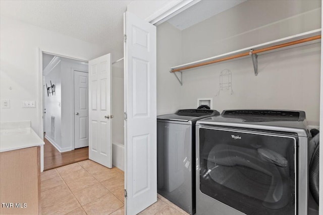 laundry room featuring light tile patterned floors, washer and clothes dryer, and a textured ceiling