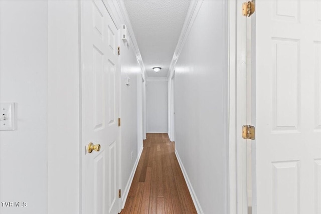 corridor with wood-type flooring, ornamental molding, and a textured ceiling