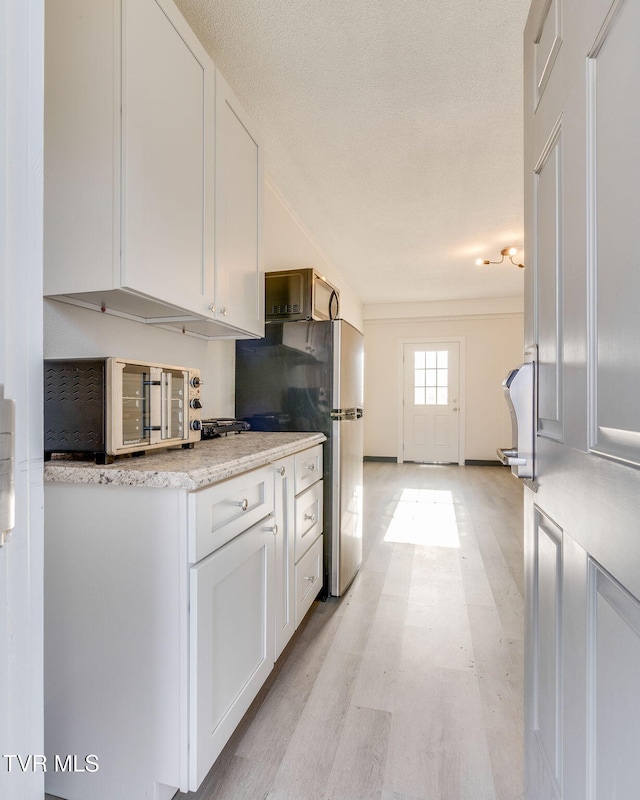 kitchen with white cabinetry, stainless steel fridge, light hardwood / wood-style floors, and a textured ceiling