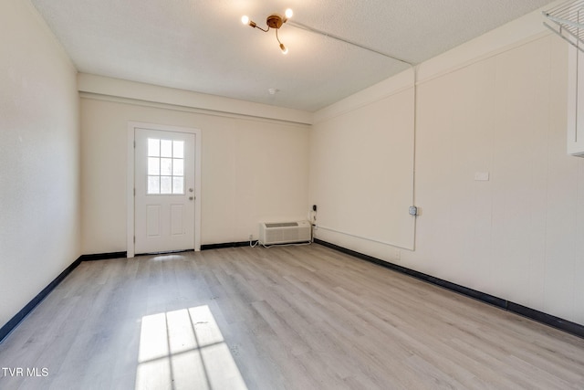 spare room with a wall mounted AC, a textured ceiling, and light hardwood / wood-style floors