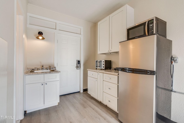 kitchen with sink, stainless steel refrigerator, light hardwood / wood-style floors, light stone countertops, and white cabinets