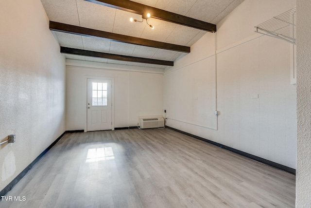 interior space featuring light hardwood / wood-style flooring, an AC wall unit, and beamed ceiling