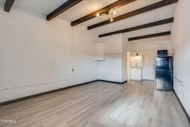 unfurnished living room featuring sink, vaulted ceiling with beams, and light wood-type flooring