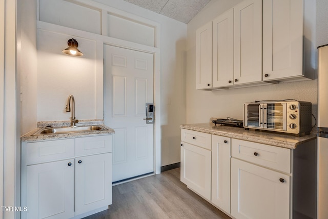 kitchen with sink, light stone counters, white cabinets, and light hardwood / wood-style floors