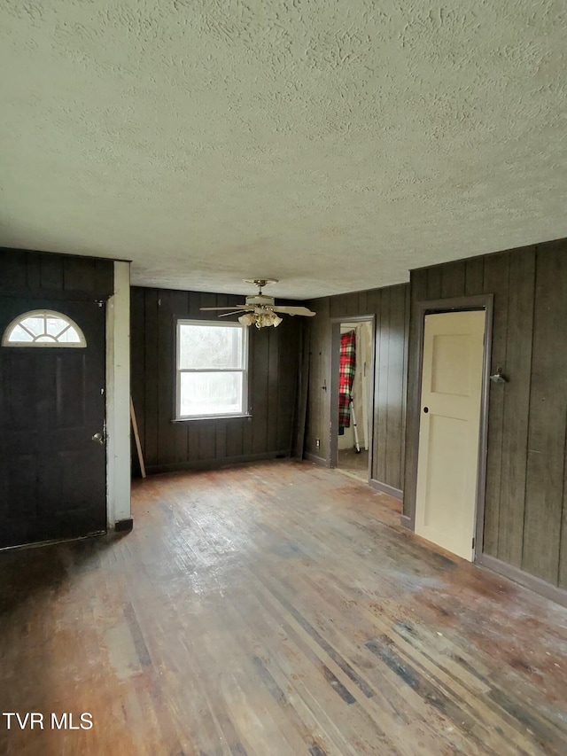 entryway featuring ceiling fan, wooden walls, light hardwood / wood-style floors, and a textured ceiling