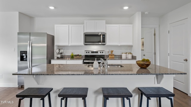 kitchen featuring sink, dark stone countertops, white cabinets, a kitchen island with sink, and stainless steel appliances