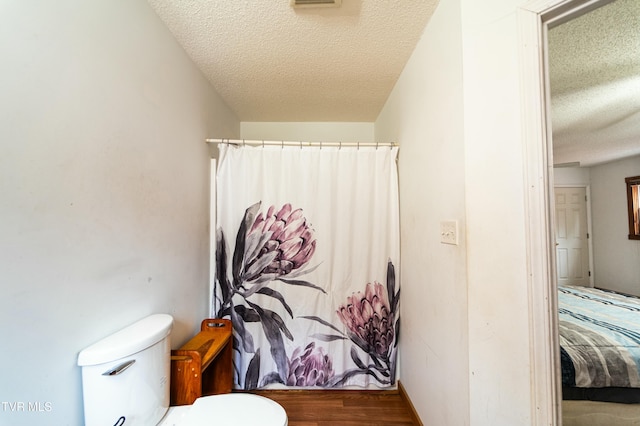 bathroom featuring hardwood / wood-style flooring, toilet, walk in shower, and a textured ceiling