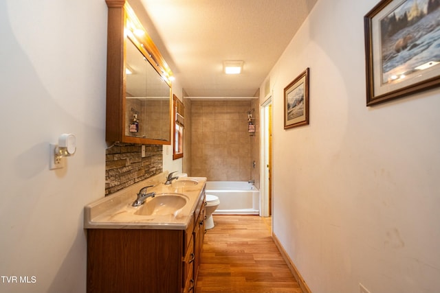 full bathroom featuring tiled shower / bath, hardwood / wood-style flooring, vanity, toilet, and a textured ceiling