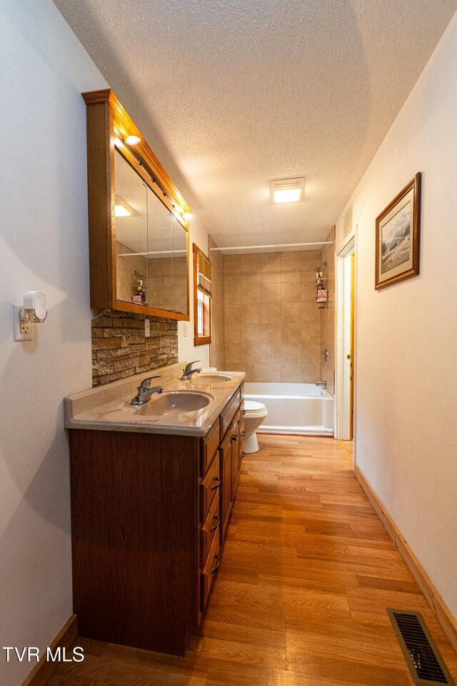 full bathroom with hardwood / wood-style flooring, vanity, a textured ceiling, toilet, and tiled shower / bath