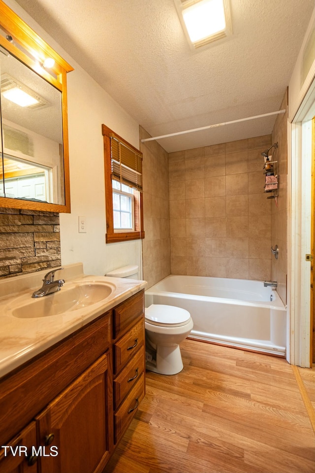 full bathroom featuring hardwood / wood-style flooring, tiled shower / bath combo, vanity, a textured ceiling, and toilet