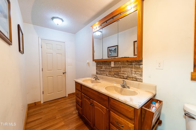 bathroom featuring hardwood / wood-style floors, backsplash, vanity, toilet, and a textured ceiling