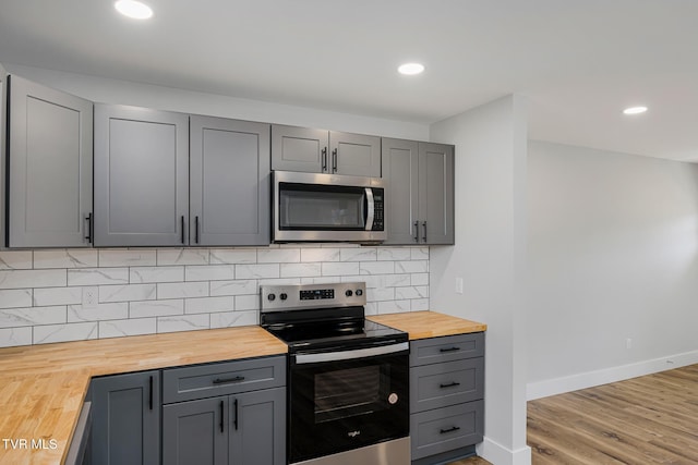 kitchen with butcher block countertops, gray cabinetry, light wood-type flooring, stainless steel appliances, and backsplash