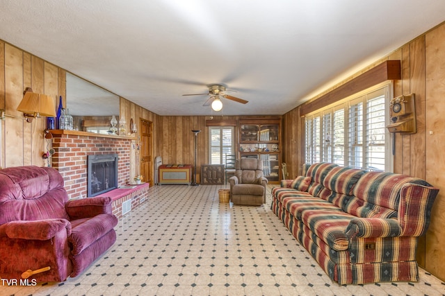 living room with ceiling fan, wooden walls, and a brick fireplace