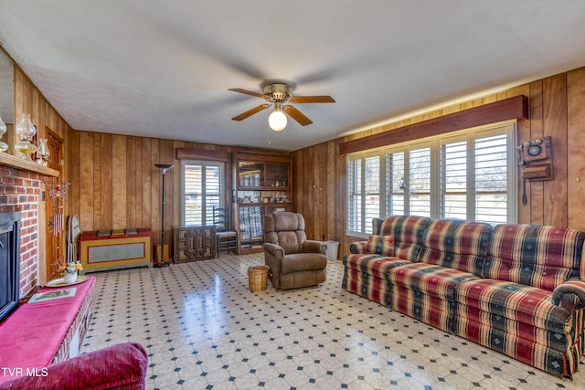 living room featuring a brick fireplace, ceiling fan, and wood walls