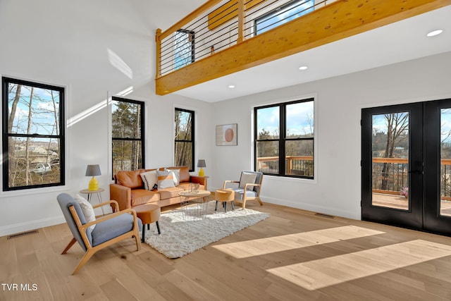 living room featuring a towering ceiling, light hardwood / wood-style flooring, and french doors