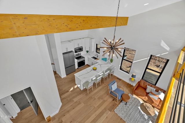 living room featuring an inviting chandelier, high vaulted ceiling, light hardwood / wood-style floors, and sink