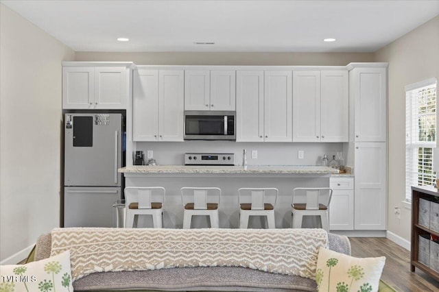 kitchen with fridge, white cabinetry, a kitchen bar, and range with electric stovetop