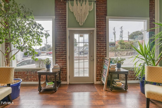 entryway with brick wall, plenty of natural light, and dark wood-type flooring