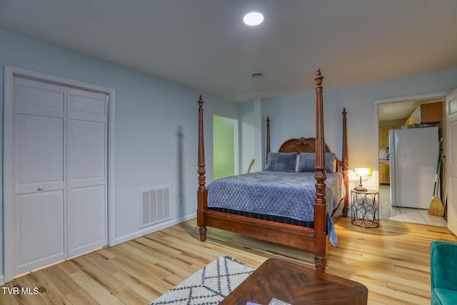 bedroom with stainless steel fridge and light hardwood / wood-style floors