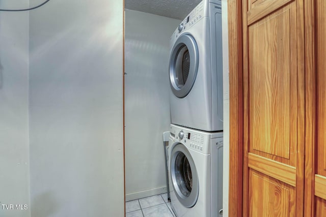 washroom with stacked washer / drying machine, light tile patterned floors, and a textured ceiling