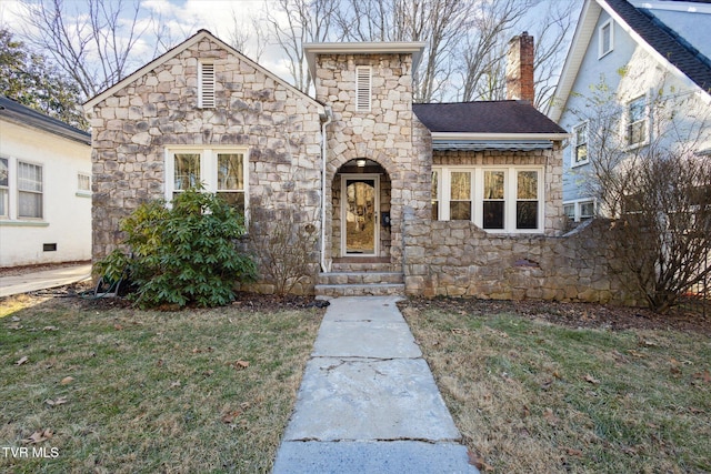 view of front facade featuring roof with shingles, a chimney, entry steps, stone siding, and a front lawn