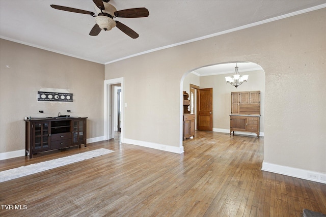 unfurnished living room with arched walkways, crown molding, ceiling fan, wood finished floors, and baseboards