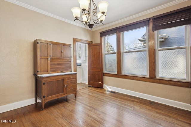 unfurnished dining area with visible vents, an inviting chandelier, ornamental molding, wood finished floors, and baseboards