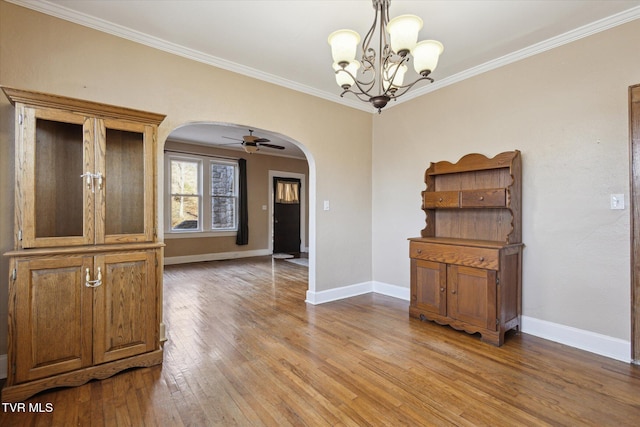 unfurnished dining area featuring light wood-style floors, baseboards, arched walkways, and crown molding