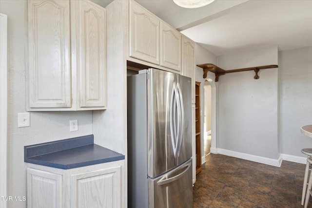 kitchen featuring freestanding refrigerator, stone finish flooring, dark countertops, and baseboards