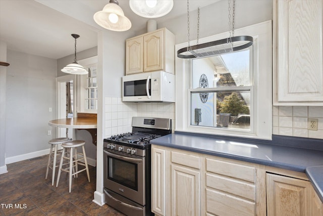 kitchen with light brown cabinetry, white microwave, dark countertops, and stainless steel range with gas stovetop