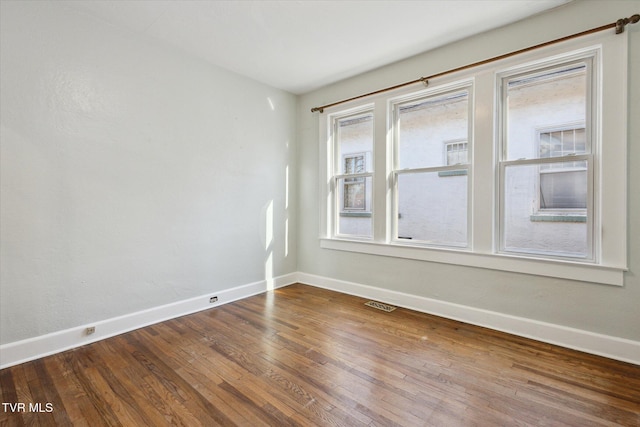 unfurnished room featuring wood finished floors, visible vents, and baseboards