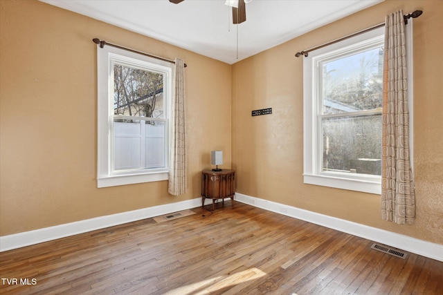 empty room with baseboards, plenty of natural light, visible vents, and wood finished floors