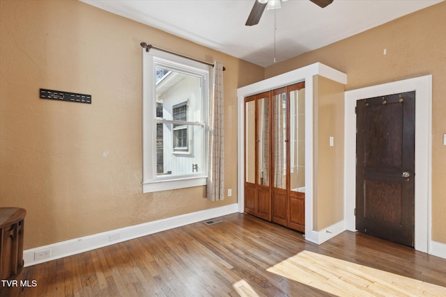 foyer with a ceiling fan, visible vents, baseboards, and wood finished floors