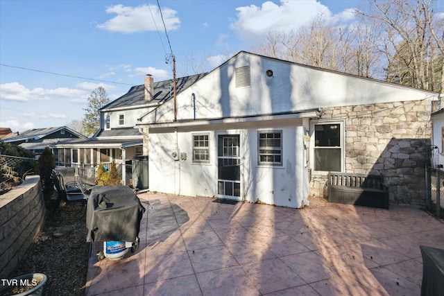 back of house with stone siding, a patio area, a chimney, and stucco siding