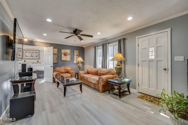 living room featuring ceiling fan, ornamental molding, a textured ceiling, and light wood-type flooring