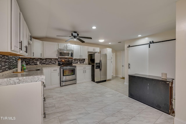 kitchen with sink, appliances with stainless steel finishes, white cabinetry, backsplash, and a barn door